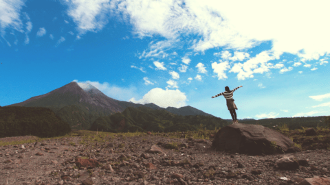 Una chica sobre una roca con los brazos abiertos contemplando un paisaje