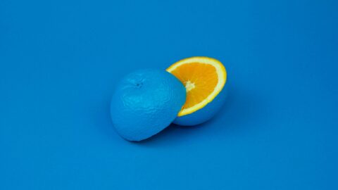 Photograph of an orange sliced in two pieces. All the picture is blue, including the skin, except the inside in orange colour.